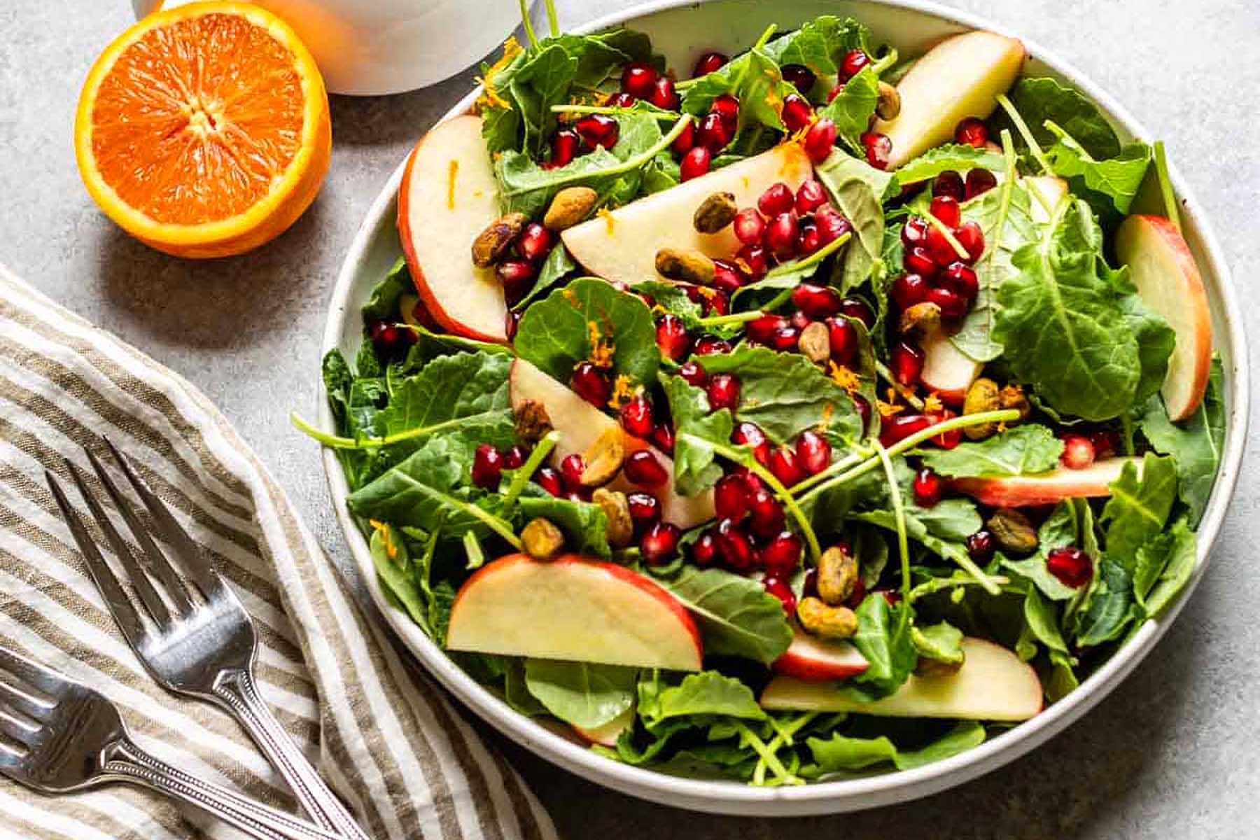 A bowl of spinach salad with apples and pomegranate.