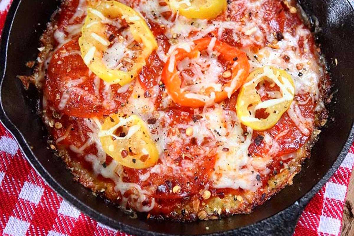 A pizza in a cast iron skillet with peppers and cheese.