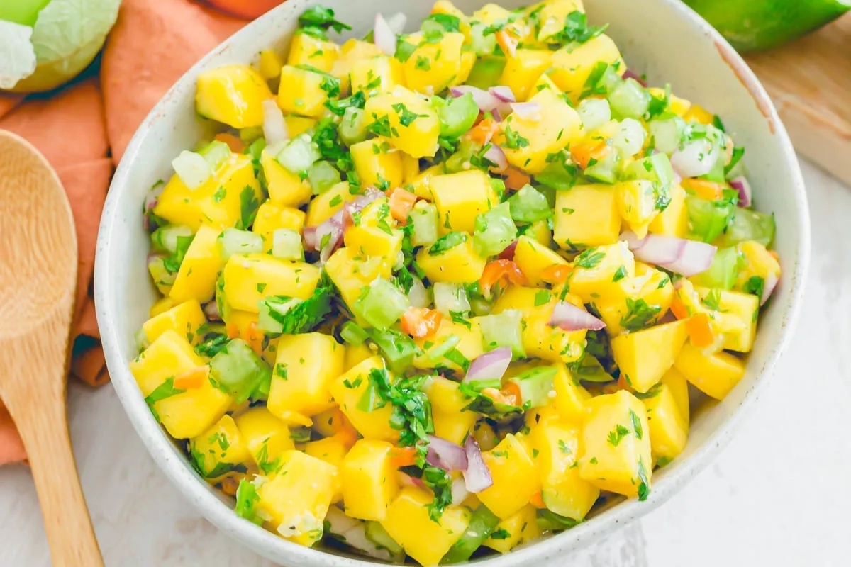 Mango salsa in a white bowl with a wooden spoon.