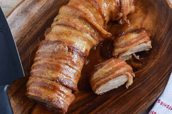 Bacon wrapped pork on a wooden cutting board.