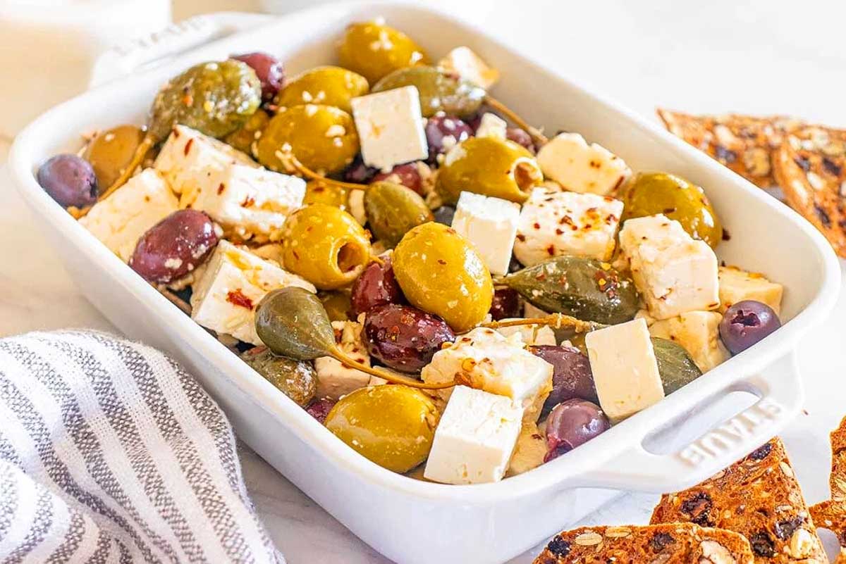 A festive white dish with olives, feta cheese and crackers, perfect for Christmas party appetizers.