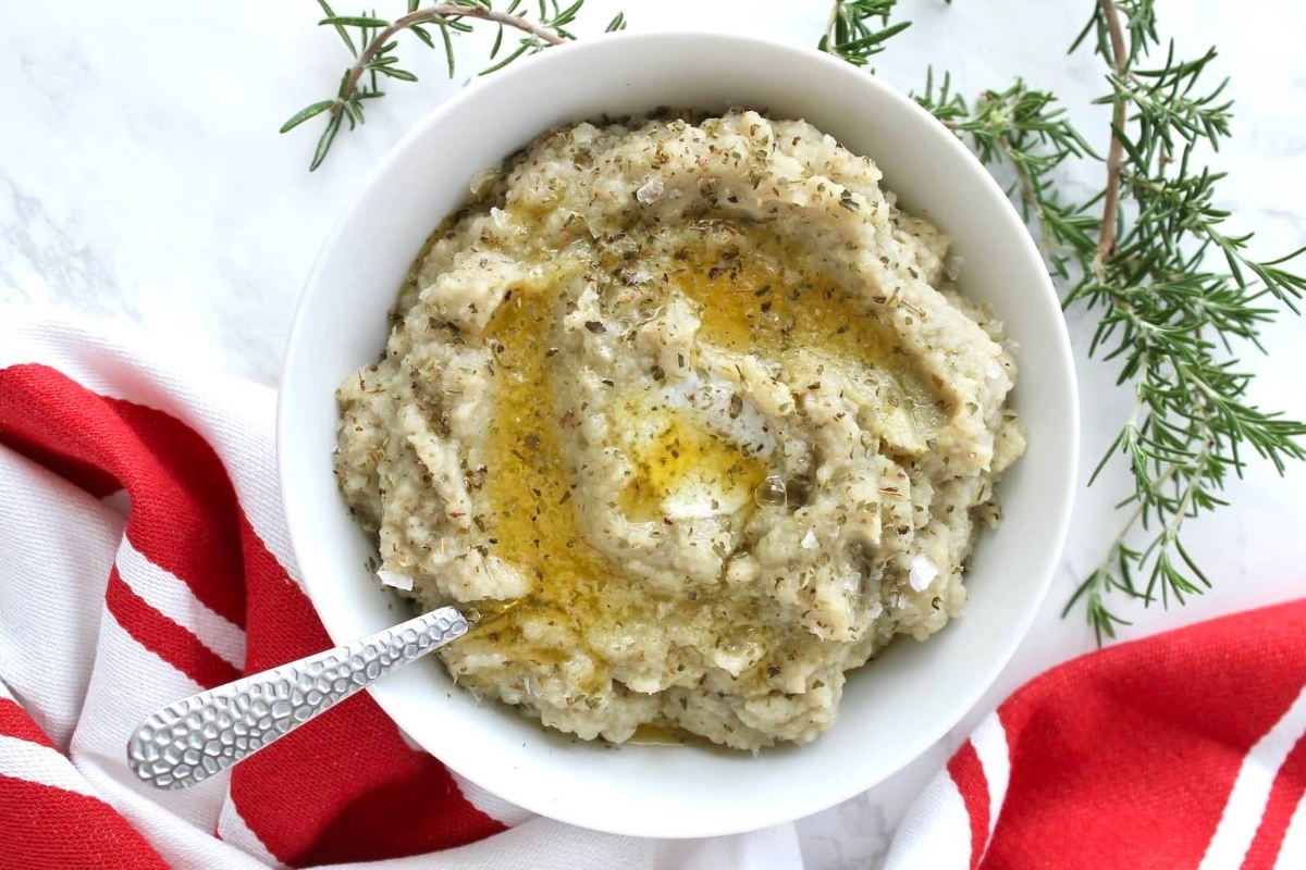 A cheap potluck Thanksgiving dish of mashed potatoes with olive oil and sprigs of rosemary.