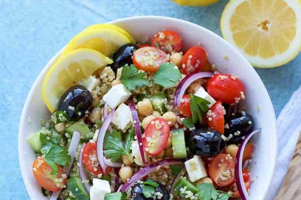 A bowl of quinoa salad with tomatoes, olives and lemons.