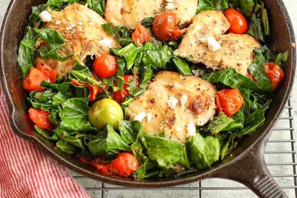 A skillet filled with chicken, tomatoes and greens.