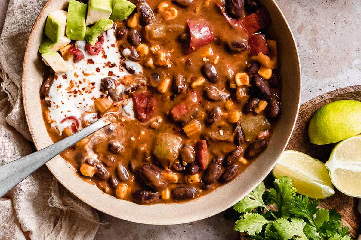 A bowl of mexican chili with sour cream and avocado.