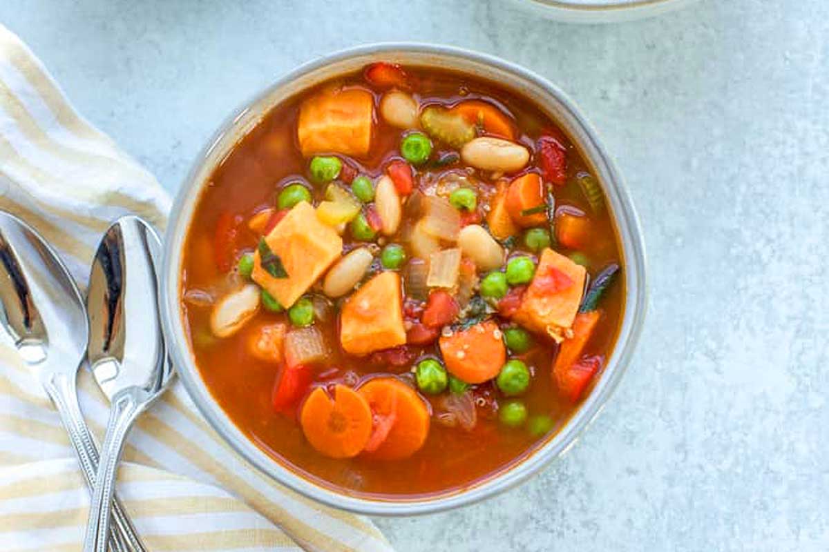 A bowl of soup with carrots, peas and beans.