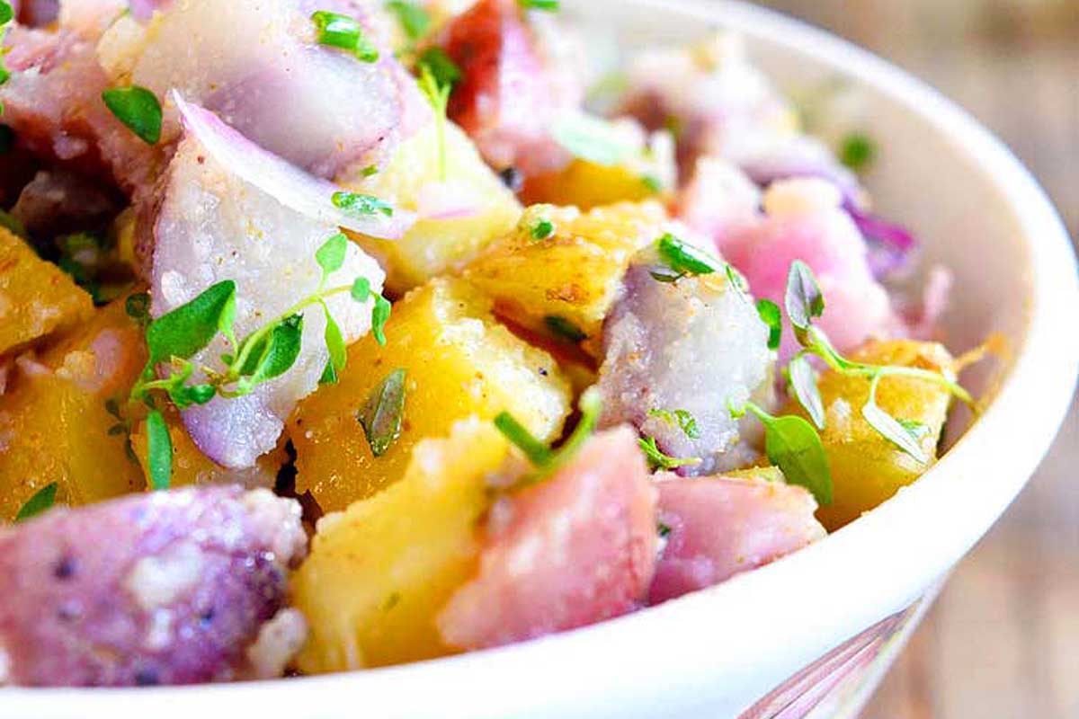 A bowl of potato salad with herbs in it.