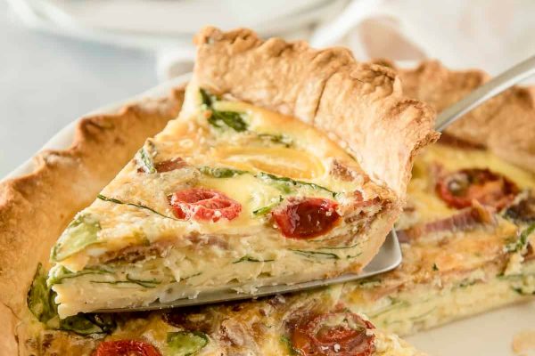 A delectable quiche recipe featuring fresh tomatoes and vibrant spinach, displayed enticingly on a plate.