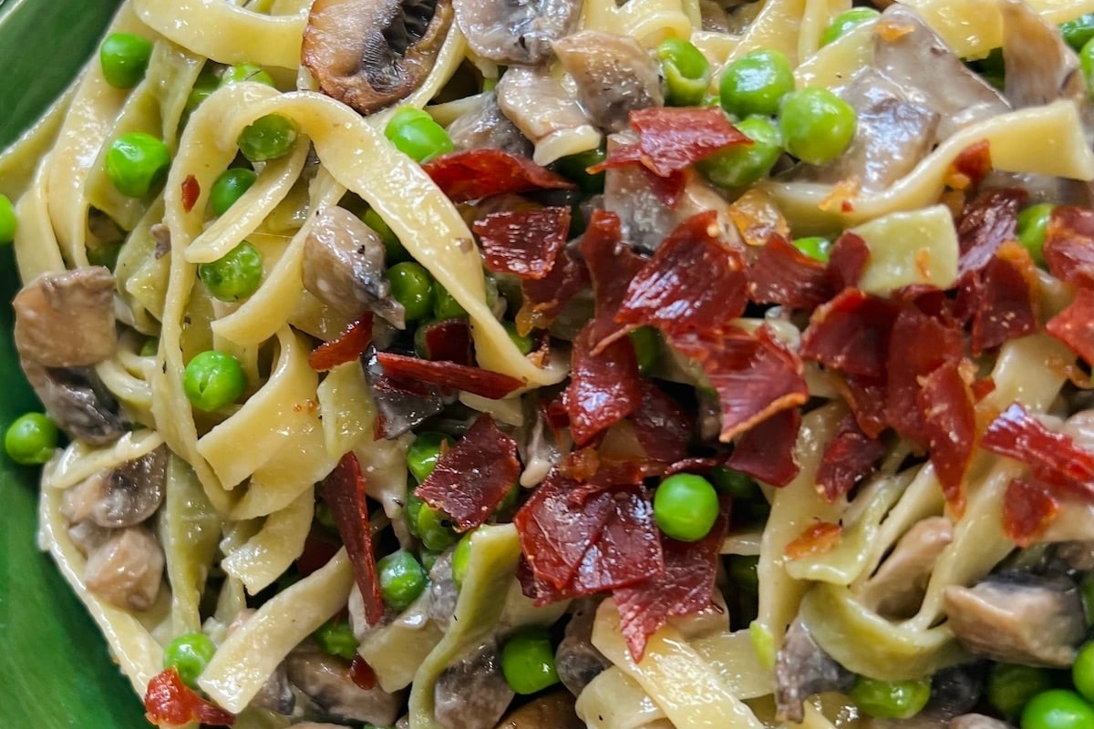 A bowl of pasta with mushrooms, peas and bacon made using frozen peas.