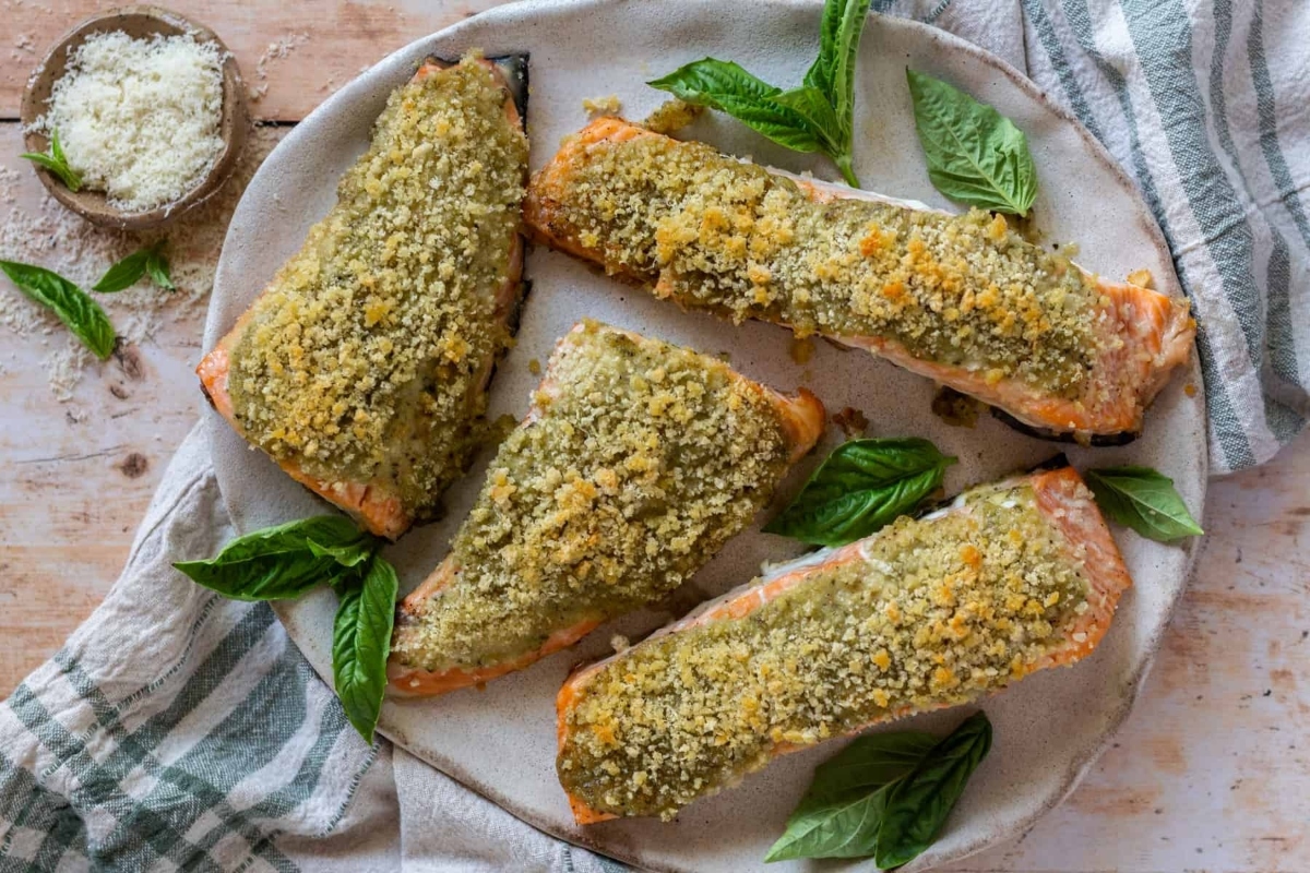 Four pesto and basil dressed salmon fillets on a plate.