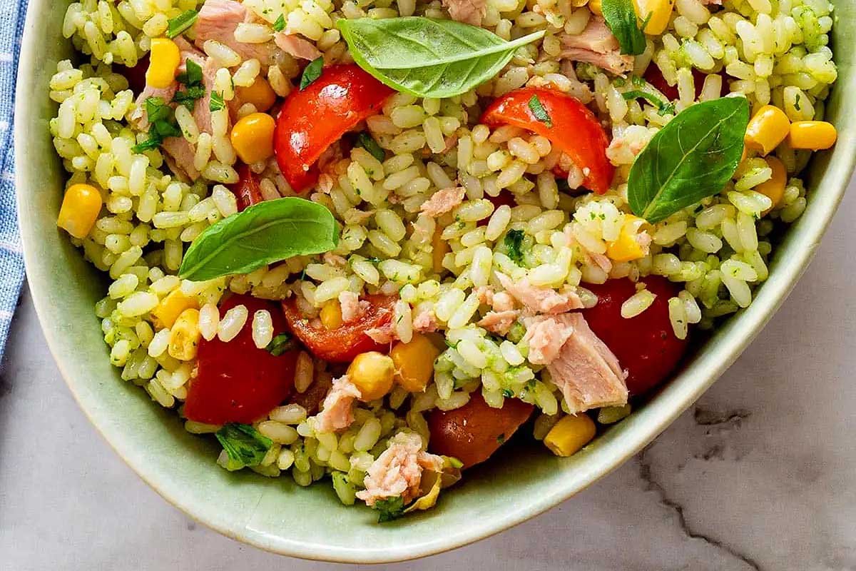 A green bowl with tuna, corn, tomatoes and basil.