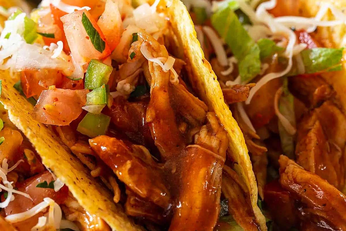 A close up of two tacos with chicken and vegetables.