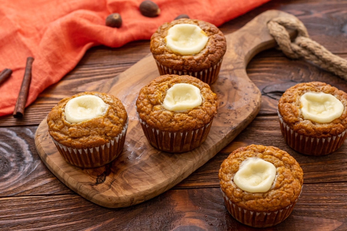Pumpkin cupcakes with cream cheese frosting on a wooden cutting board, perfect for Holiday Recipes.