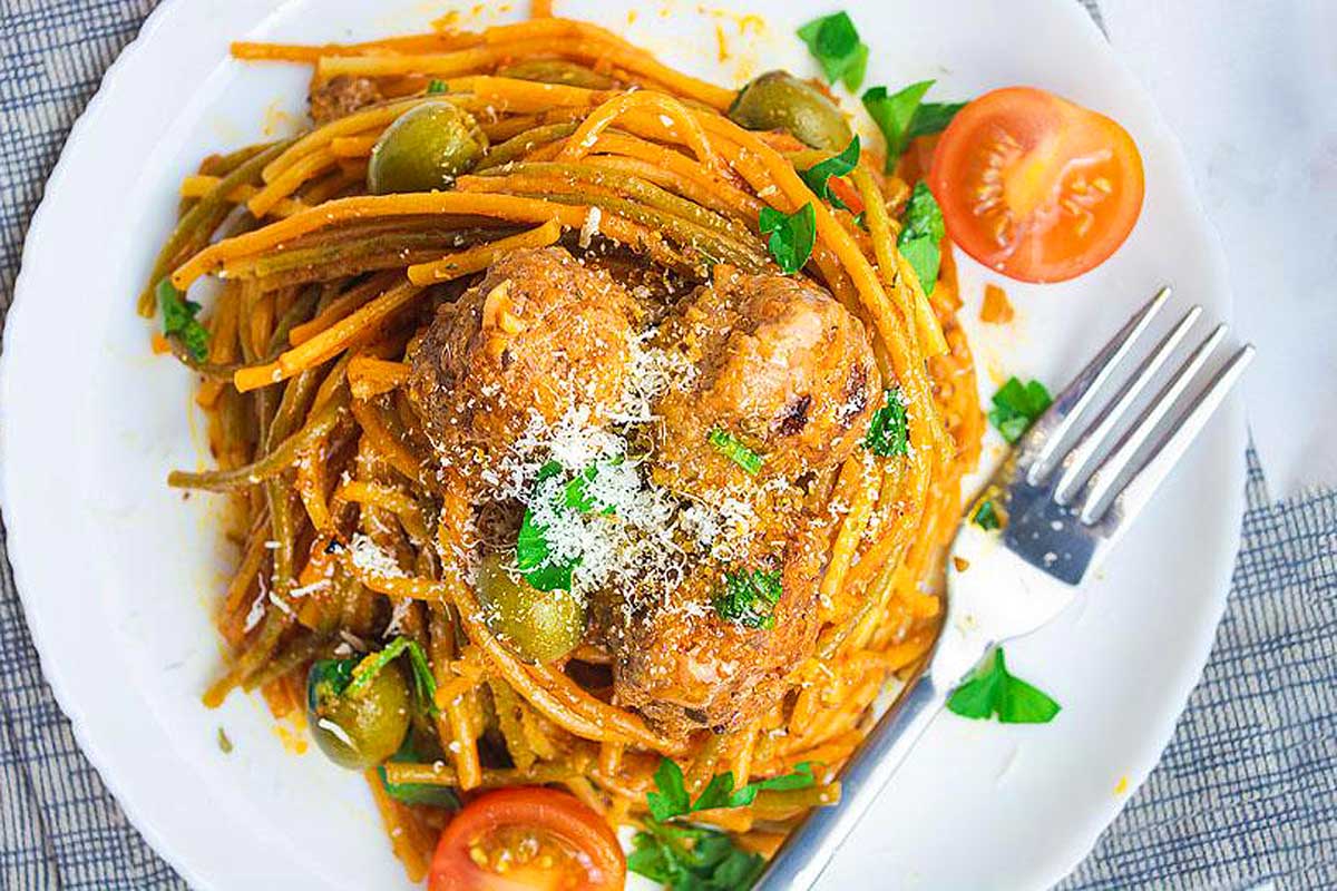 A plate of spaghetti with chicken and tomatoes on it.