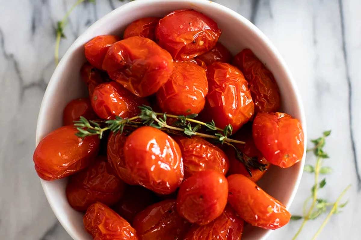 Aromatic roasted tomatoes showcased in a pristine white bowl, garnished elegantly with thyme.