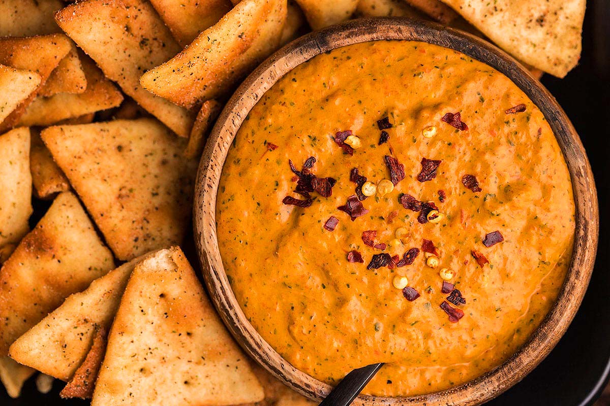 A bowl of red pepper dip with pita chips.