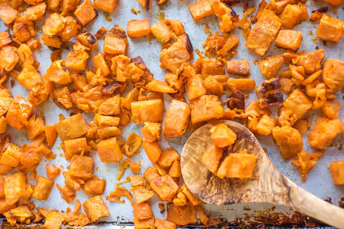 Sweet potatoes on a baking sheet, roasted to perfection with a wooden spoon.