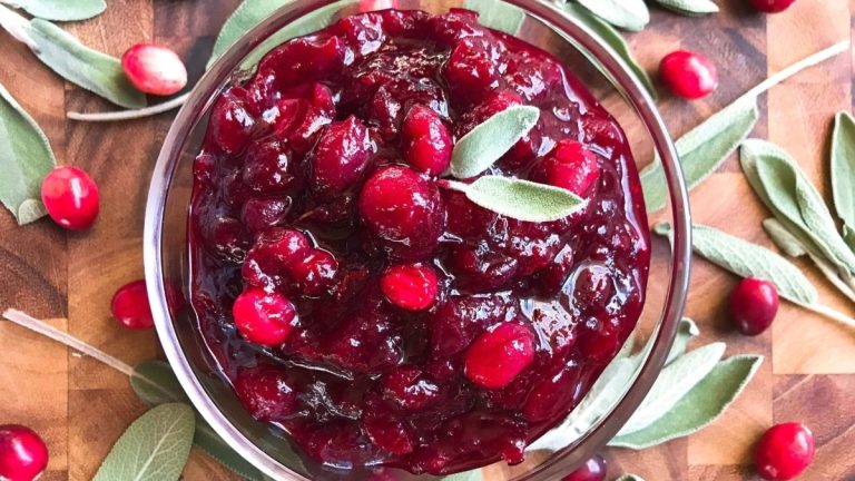 Delicious cranberry sauce recipe with sage leaves on a cutting board.