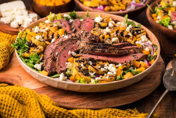 A bowl of steak salad with mangoes and feta cheese.