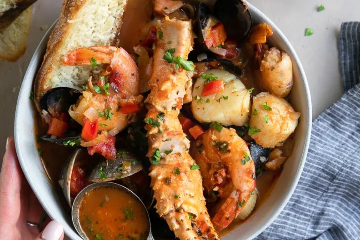 A bowl of seafood stew with bread and clams, ideal for a main course.