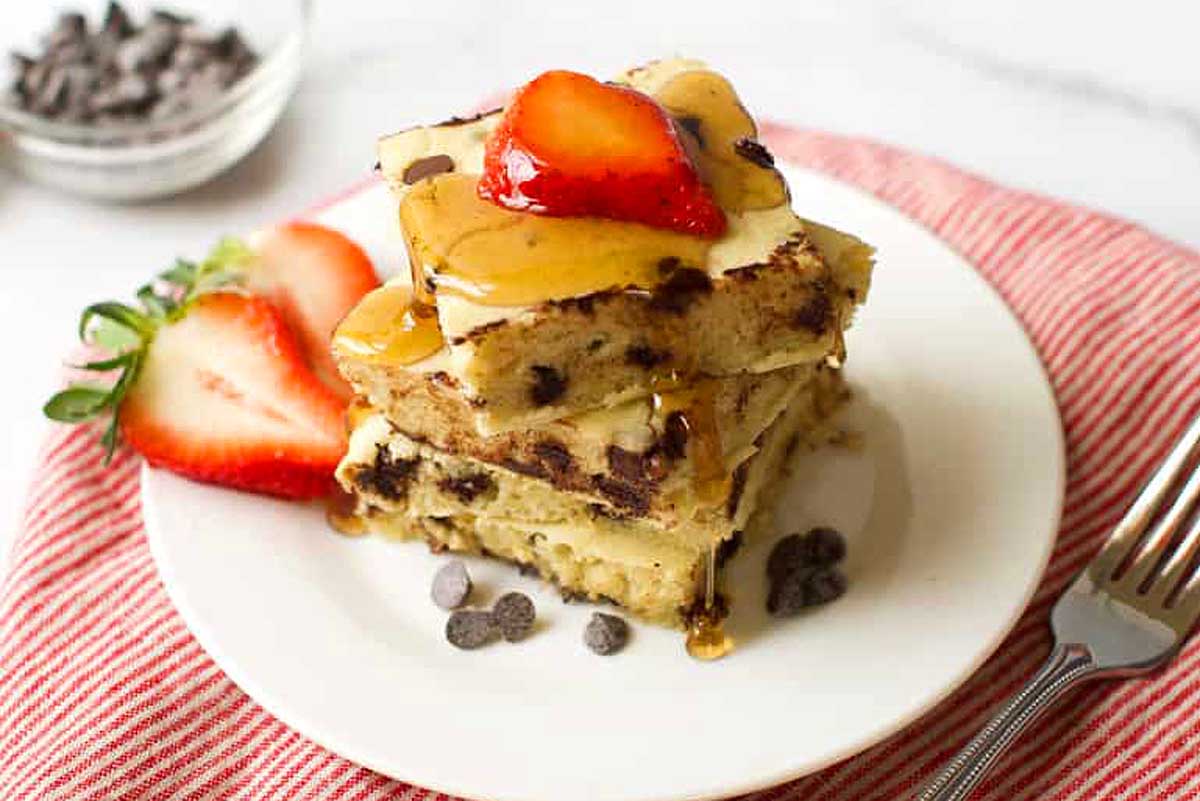 A stack of chocolate chip pancakes with strawberries on top, perfect for a delicious brunch.
