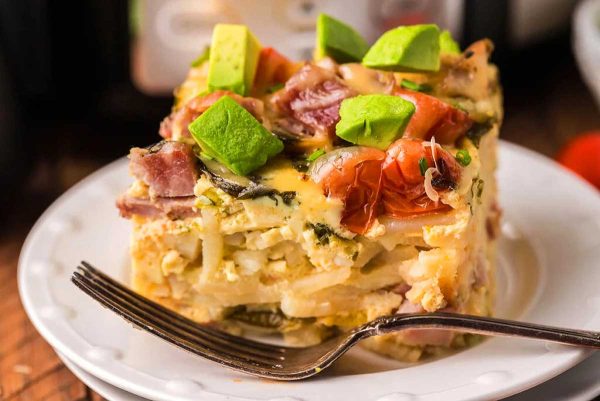 A delicious slice of breakfast casserole perfect for brunch on a plate with a fork.