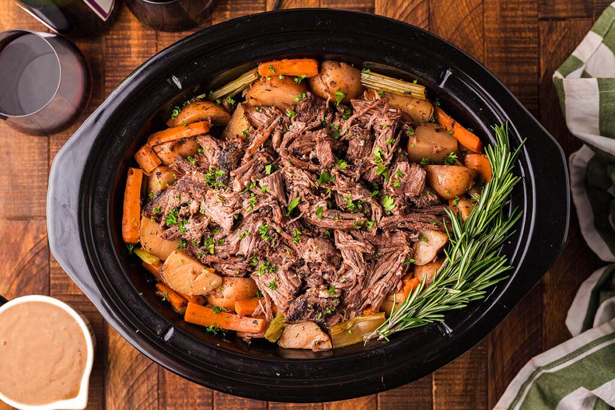 A crock pot full of roast beef, carrots and potatoes, perfect for Thanksgiving mains.