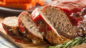 Delicious meatloaf recipe displayed on a cutting board, accompanied by ketchup and carrots.