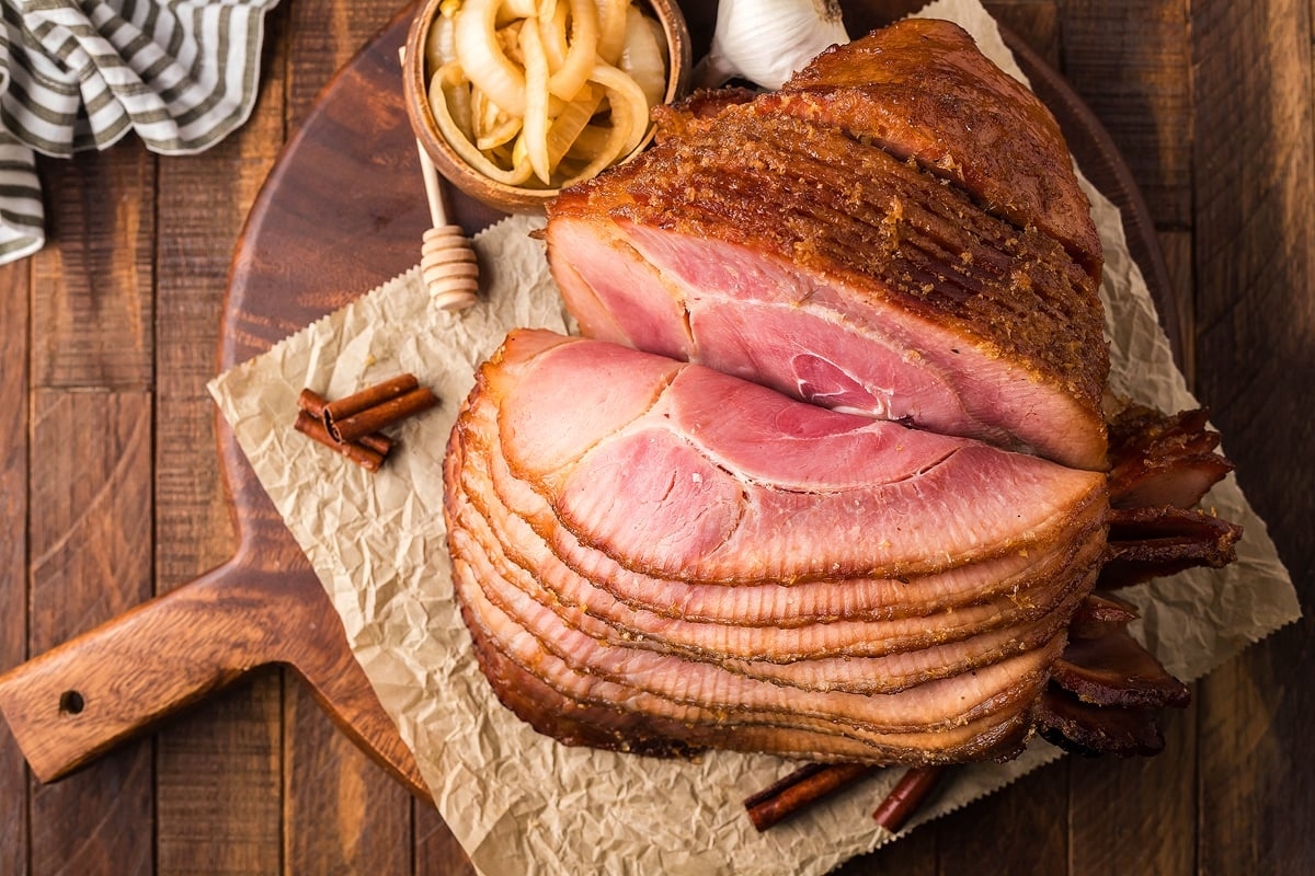 A ham, a traditional Thanksgiving main dish, is sitting on a wooden cutting board.