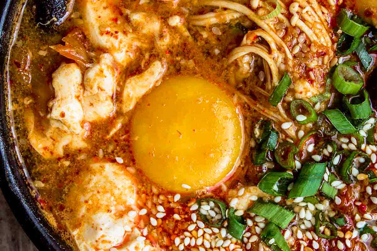 A bowl of korean noodle soup with an egg on top.