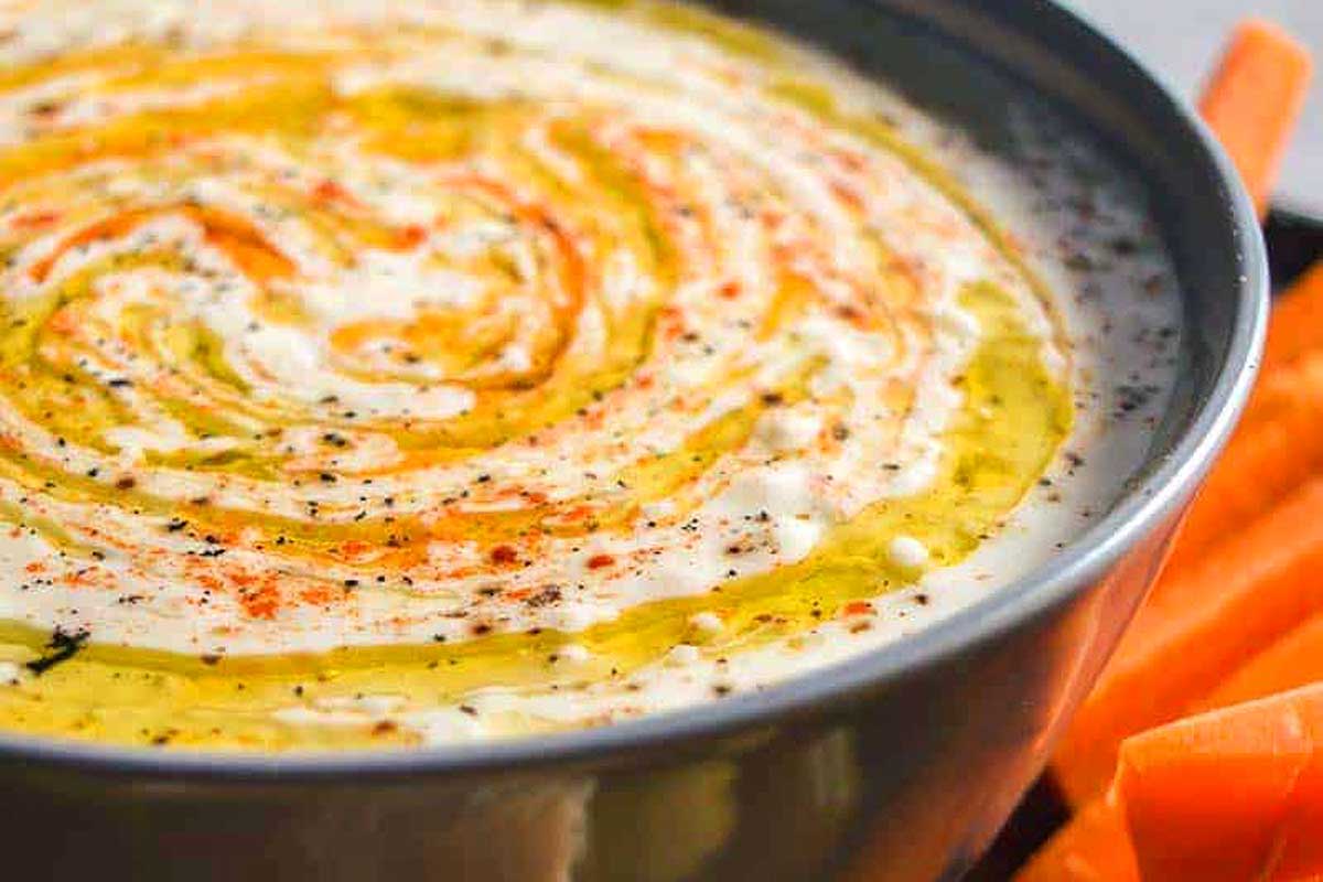 A bowl of hummus with carrots in it.