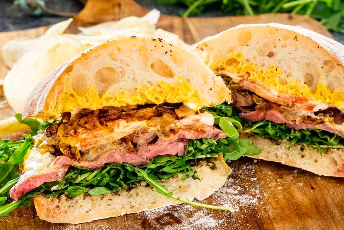A sandwich with pesto and greens on a wooden cutting board.
