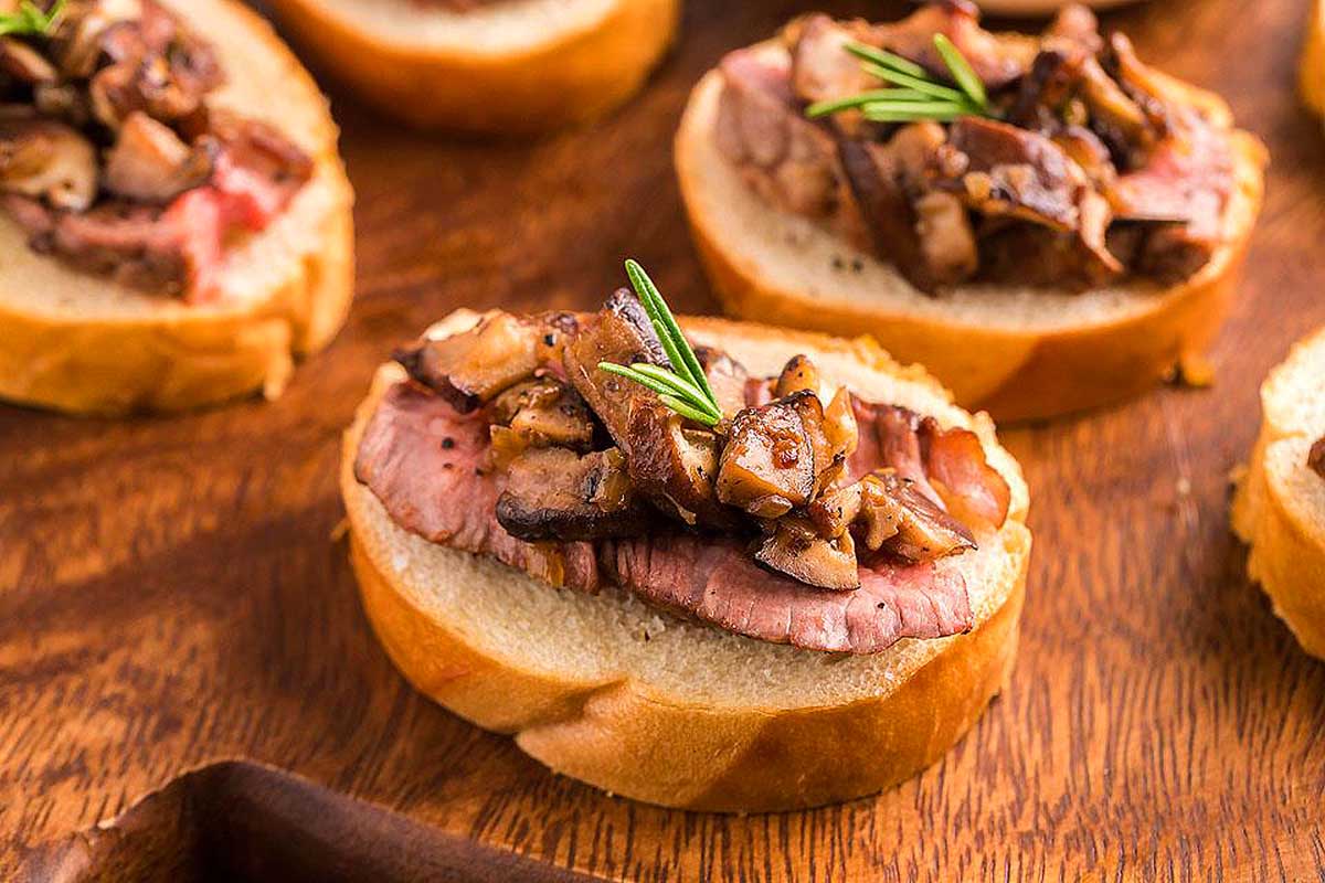 Beef and mushroom crostini, perfect for any occasion, beautifully displayed on a wooden cutting board with rosemary sprigs.