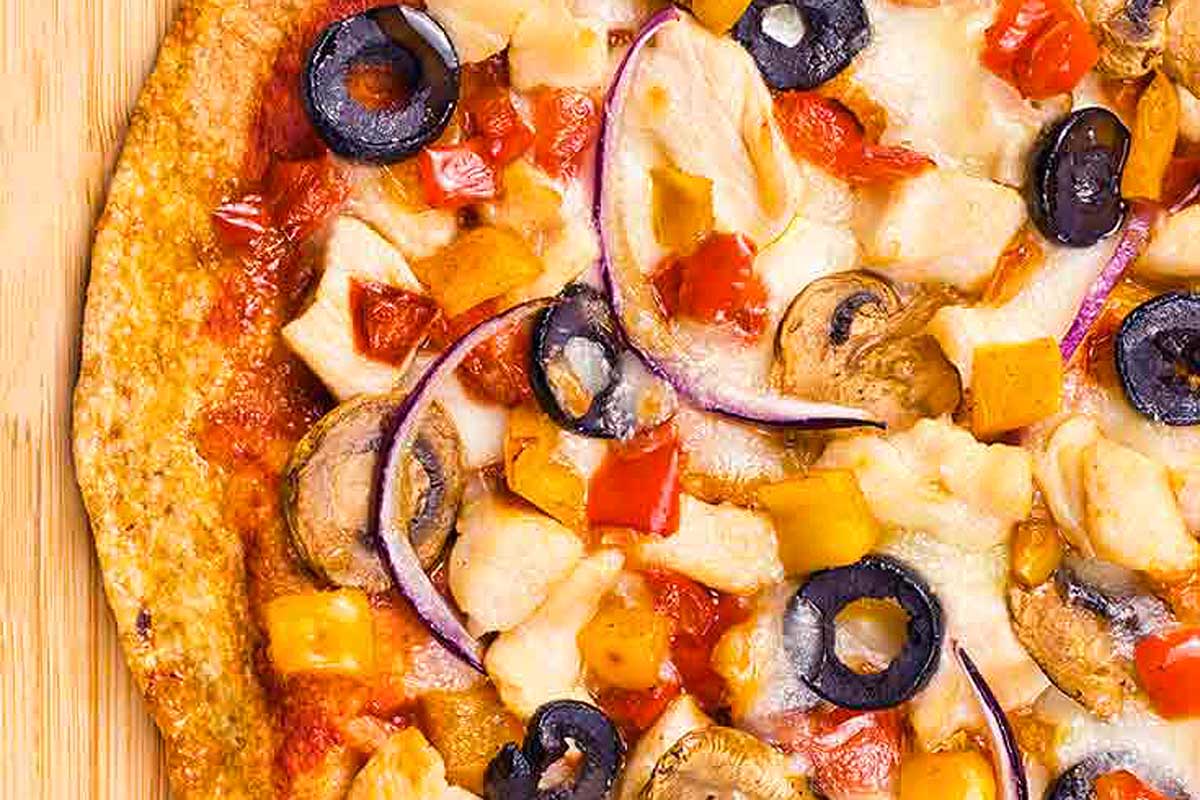 A pizza with chicken, olives, onions and peppers on a wooden board.