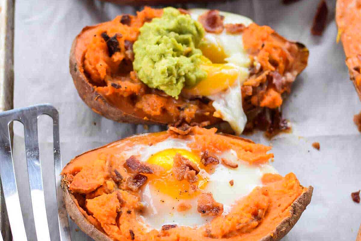 Sweet potatoes with eggs and guacamole on a baking sheet.