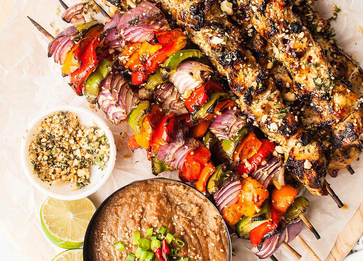 Skewered chicken with a delicious dipping sauce, presented on a rustic wooden board. This is one of the best skewer recipes.