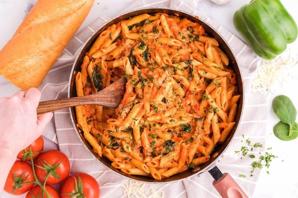 A delicious and simple recipe for penne pasta with pantry staples like spinach and tomatoes, cooked to perfection in a pan and stirred with a wooden spoon.