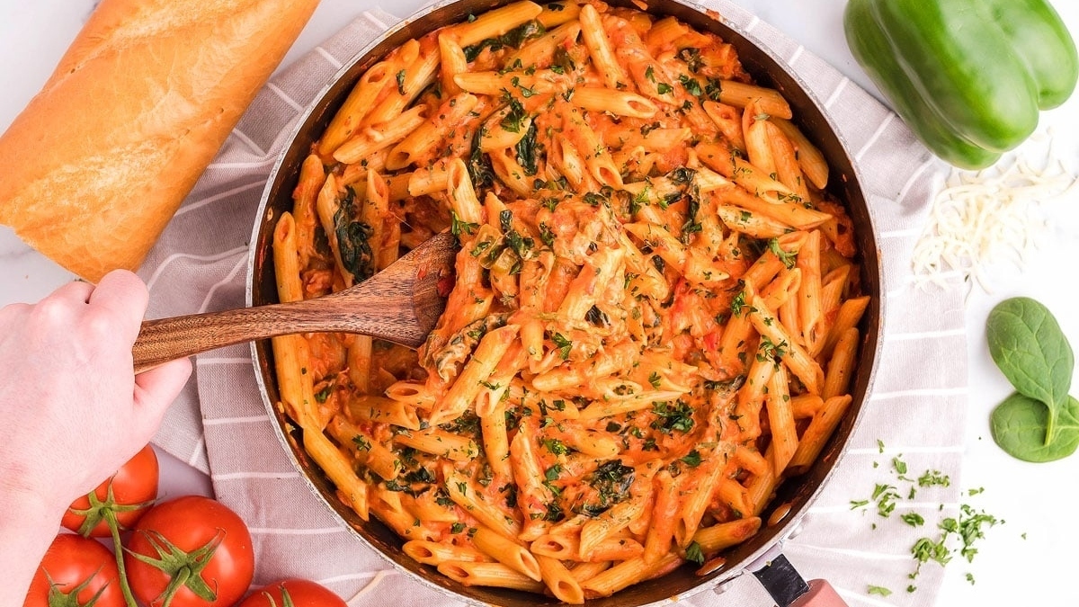 A quick and easy recipe using pantry staples, this flavorful penne dish combines spinach and tomatoes, cooked to perfection in a pan and stirred with a trusty wooden spoon.