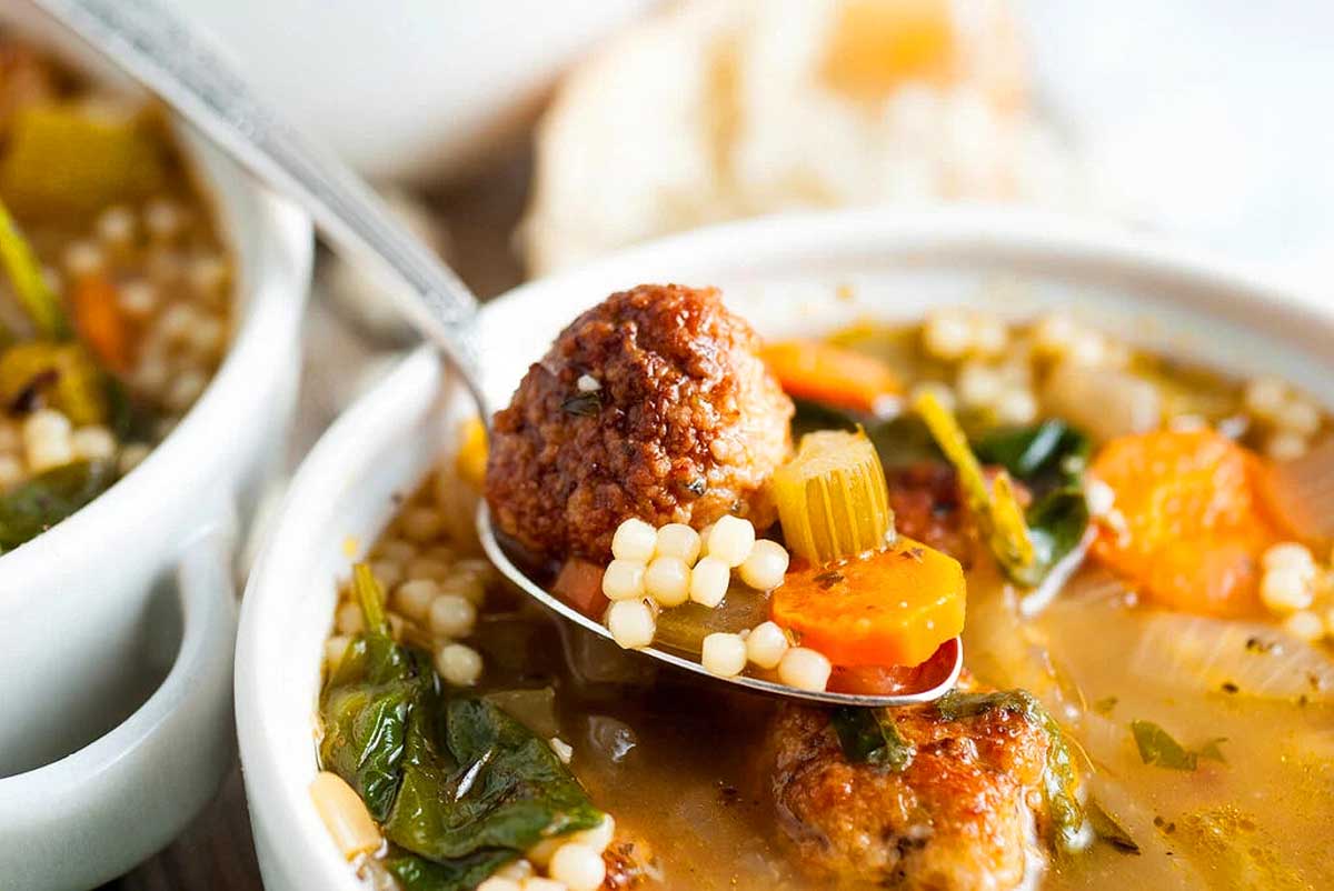 Two bowls of soup with meatballs and vegetables.