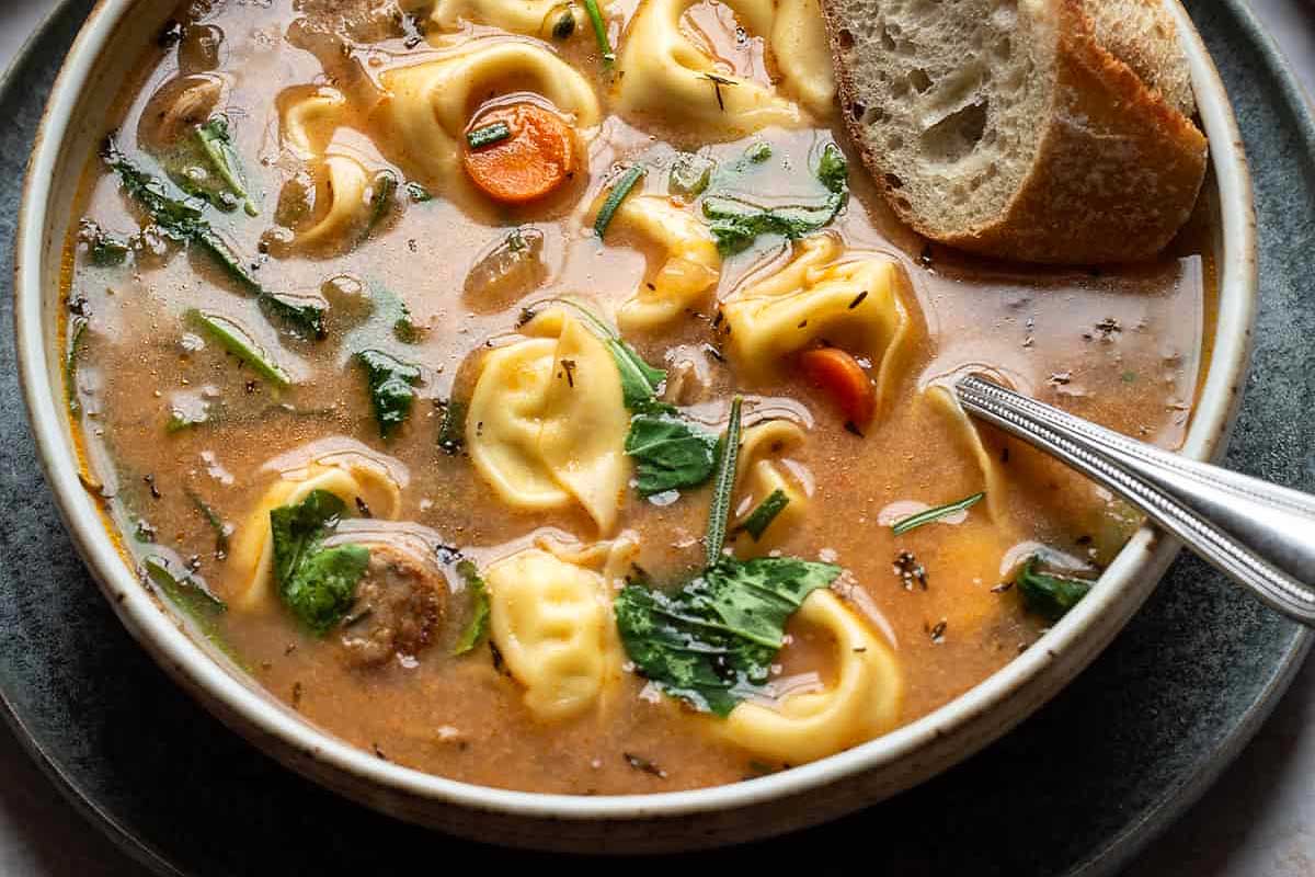 A bowl of tortellini soup with bread and spinach.