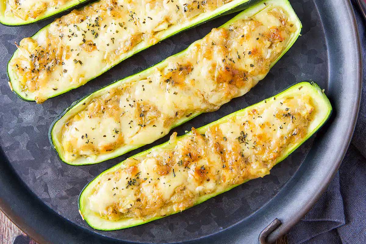 Four grilled zucchini boats on a black plate.