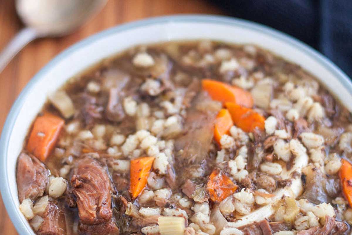 A Slow Cooker Soup: A bowl of beef and barley soup on a wooden table.