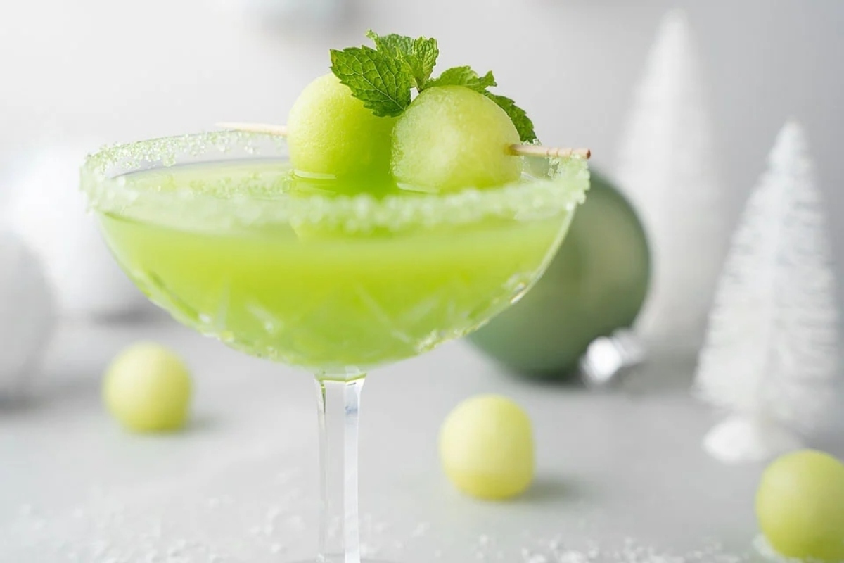 A festive Grinch martini recipe featuring a green hue and vibrant melon and mint garnishes.