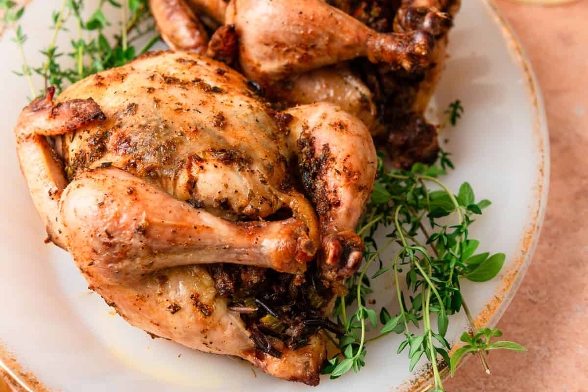 Two roasted chickens on a plate with Thanksgiving herbs.