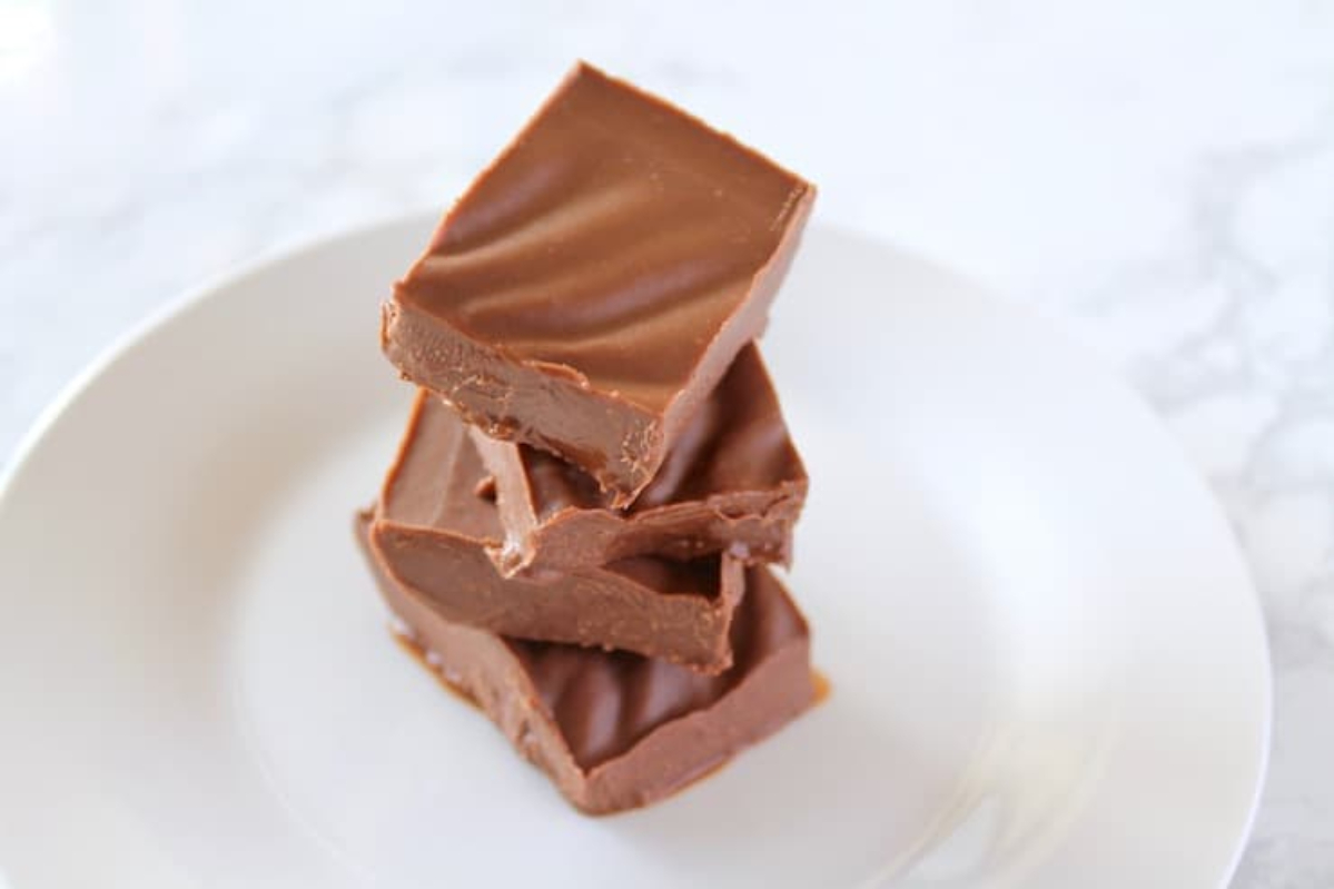 A stack of chocolate fudge, perfect for Christmas candy recipes, on a white plate.