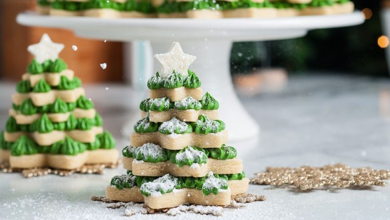 Sugar cookies cut out in the shape of Christmas trees arranged on a white plate.