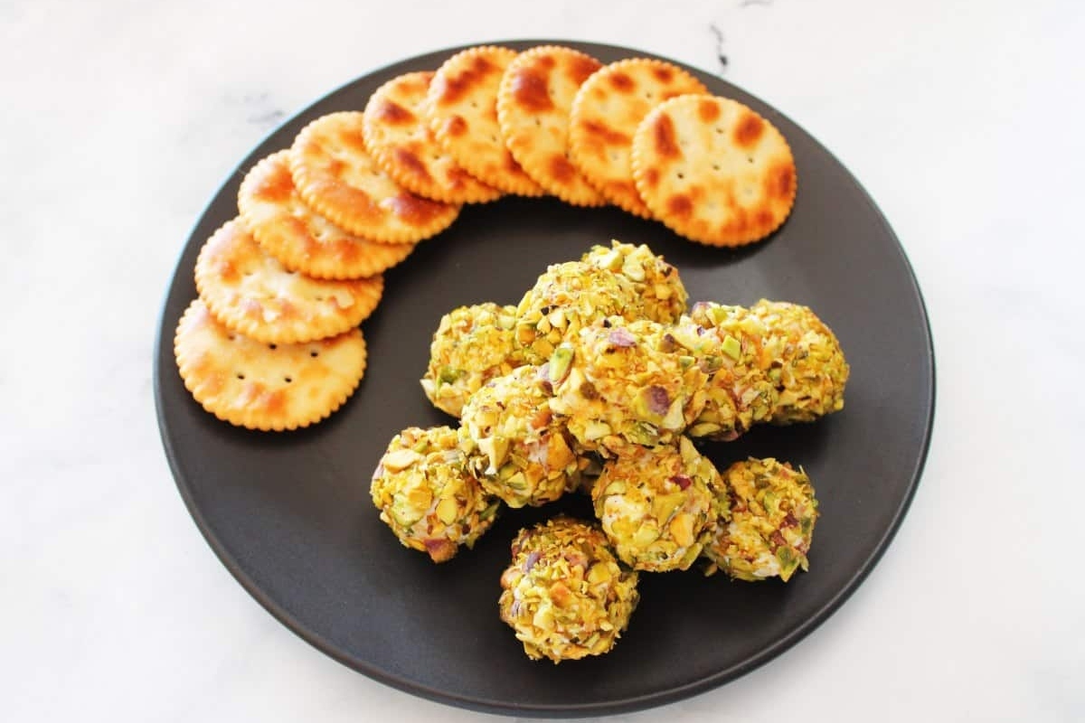 Goat cheese pistachio meatballs on a black plate with crackers, perfect for appetizers.