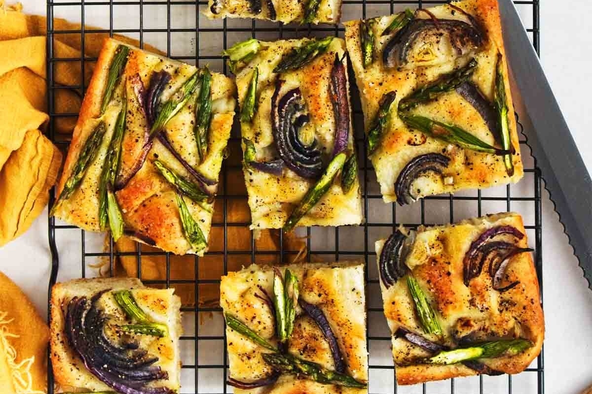 Four slices of asparagus and onion pizza on a focaccia cooling rack.