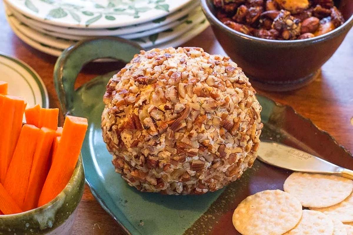 Festive cheese ball served with crackers and carrots on a plate.