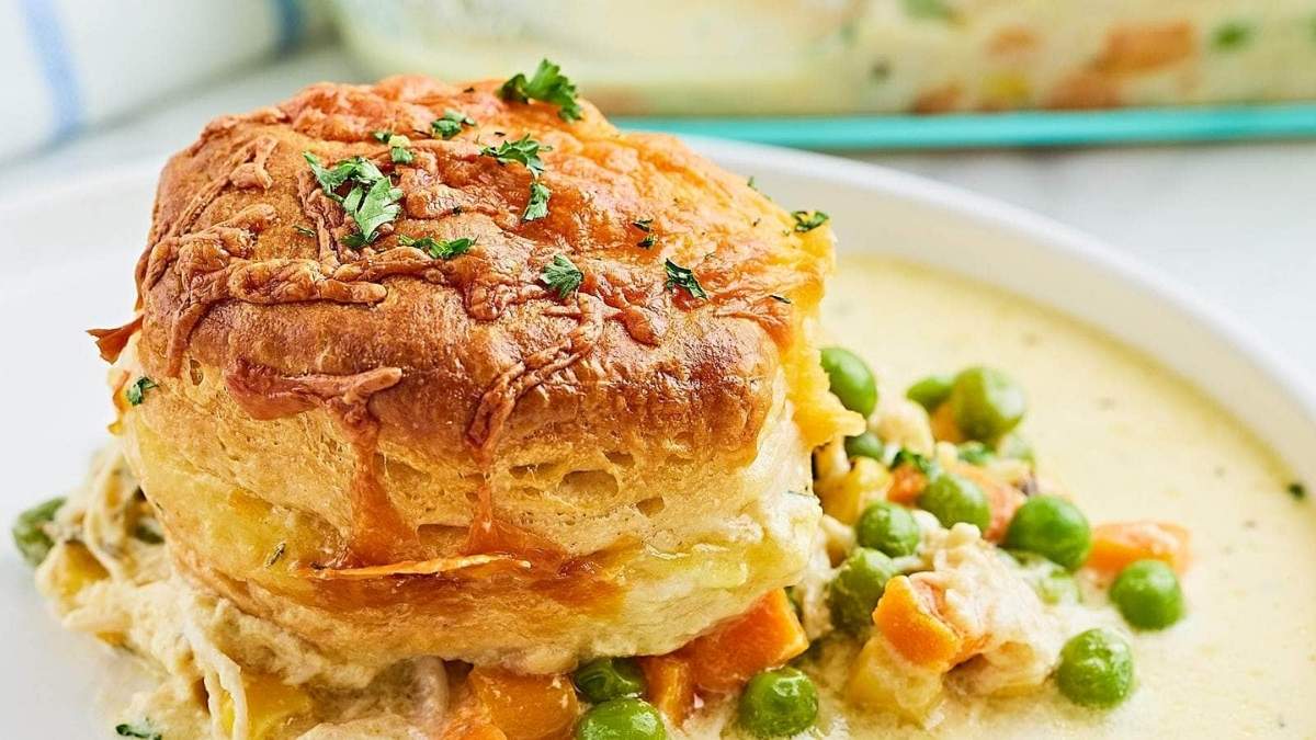 Comfort food recipe for chicken pot pie on a plate with peas and carrots.